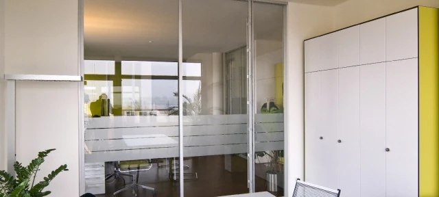 Modernes Büro mit Glastrennwand, weißen Schränken und Pflanzen für Arbeitsumgebung.