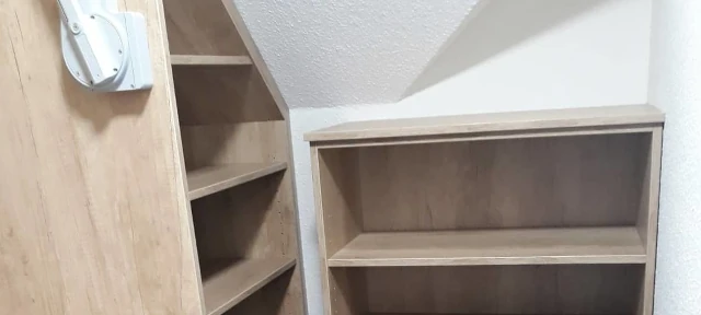 Zwei Holzregale mit Ablageflächen stehen unter einer schrägen Zimmerdecke im Raum.