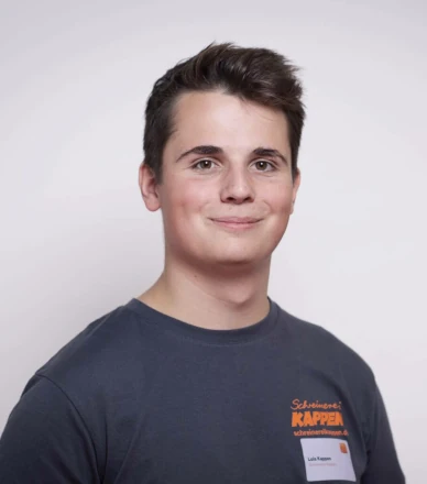 Junger Handwerker mit dunkelblauem T-Shirt und Firmenlogo der Schreinerei blickt freundlich.