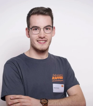 Junger Mann mit Brille und T-Shirt einer Schreinerei steht vor weißem Hintergrund.